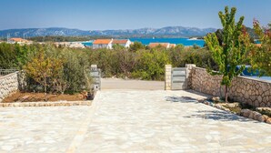 A paved pathway leading to a gated entrance with stone walls and a view of a coastal area with buildings and mountains in the background. - Amazing home in Murter with sauna (Murter)