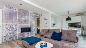 Un salon moderne avec un mur à motifs, un canapé, une table basse agrémentée de vases bleus et, au fond, un coin cuisine.