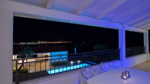 Un balcon avec une piscine, une balustrade transparente et une vue sur un bâtiment illuminé au loin.