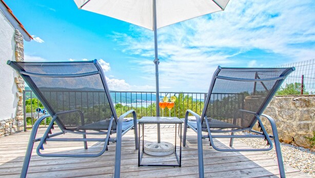 Une terrasse avec deux chaises et une table, un parasol et une vue sur l’océan.