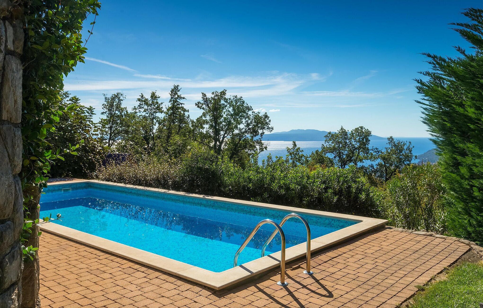 Une piscine rectangulaire avec des rampes métalliques, entourée d’une terrasse en briques.