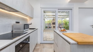 Una cocina moderna con microondas integrado, encimera de madera y puerta corredera de vidrio que da a un espacio exterior con chimenea de piedra y una silla colgante.