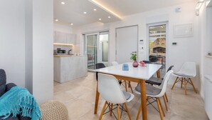 Cocina moderna con zona de comedor, que incluye una mesa blanca, sillas grises y una pequeña isla con microondas.