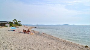 Una playa de guijarros con gente tomando el sol y nadando.