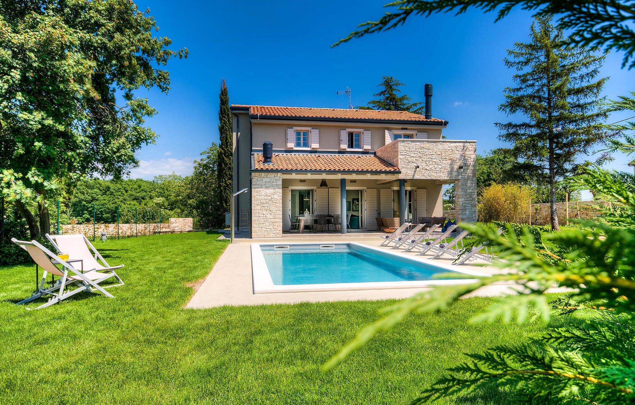 Une maison à deux étages dotée d’une piscine, d’un patio avec des chaises longues et d’une façade en pierre.