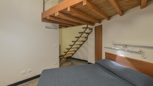 Ein Schlafzimmer mit einem Bett, Holzboden, einer Treppe und einem an der Wand befestigten Regal.