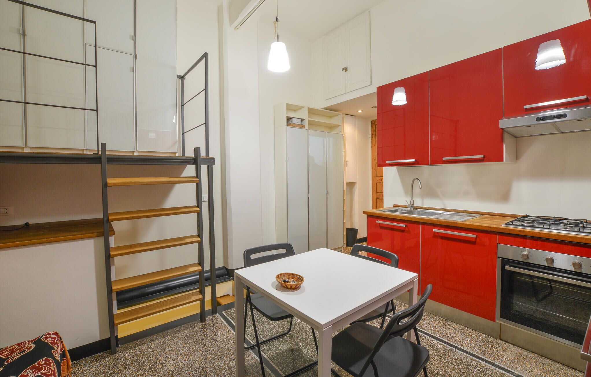 Een kleine keuken met een rode aanrecht, een witte tafel en een fornuis.