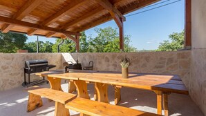 An outdoor wooden table with benches, a grill, and a chair under a wooden roof. - Amazing home in Tinjan (Tinjan)