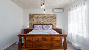 A bedroom with a stone wall, wooden bed frame, two bedside tables, and a window with sheer curtains. - Amazing home in Tinjan (Tinjan)