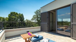A modern balcony with a wooden table and blue cushioned seating, a glass door leading to an outdoor area, and a view of trees and sky. - Awesome home in Novigrad (Novigrad)