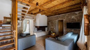 Ein rustikales Interieur mit Steinwand, Holzbalkendecke, einer Treppe, einem Kamin und einem Flachbildfernseher.