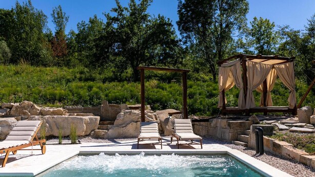 Ein Poolbereich mit Liegestühlen, einer Holzpergola und einem Sonnensegel.