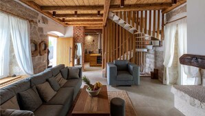 Ein rustikales Interieur mit freiliegenden Holzbalken, einer Steinwand, einer Treppe und einer gemütlichen Sitzecke mit Couchtisch.