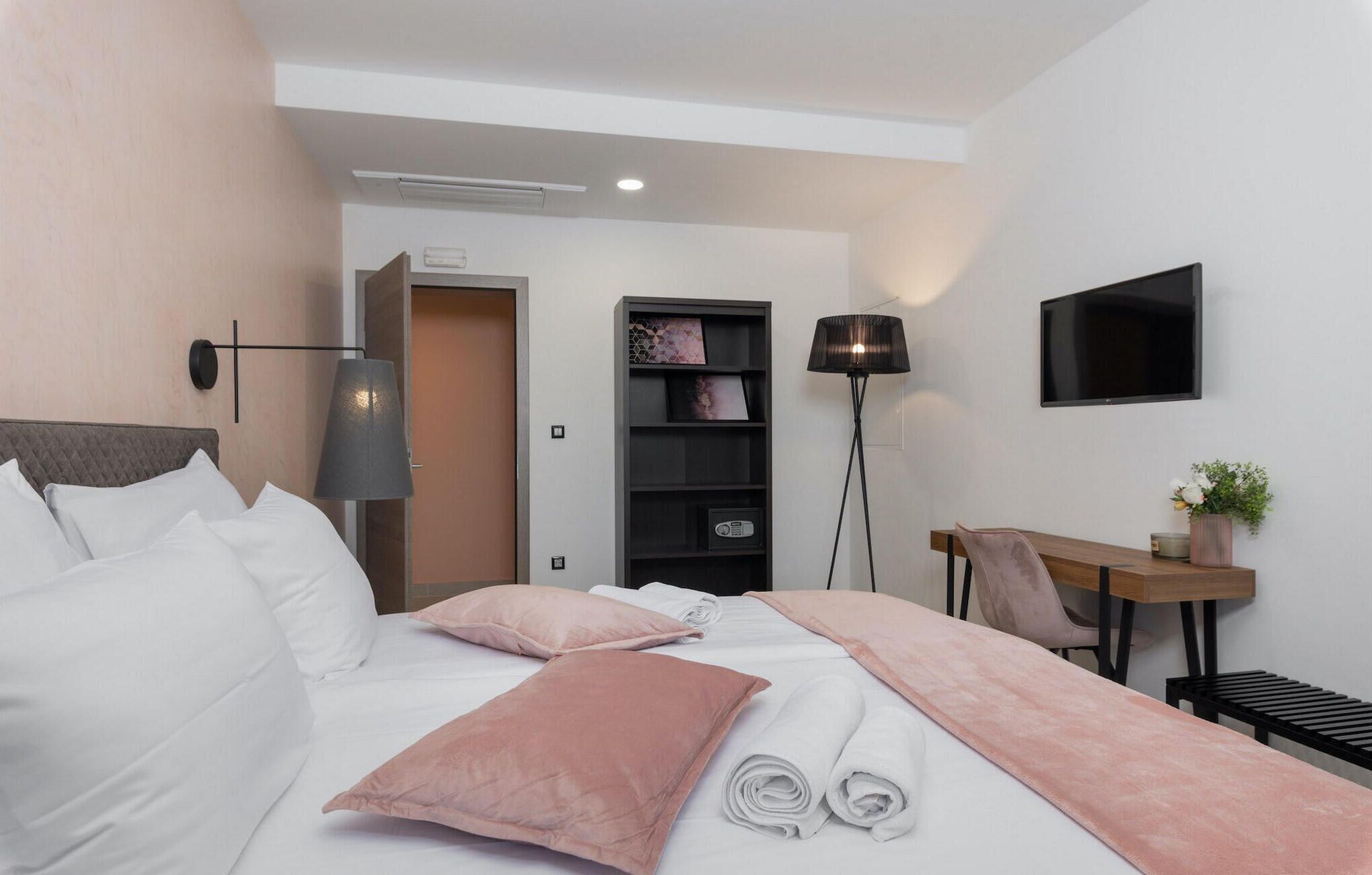 A modern hotel room with a bed, bedside table, lamp, and a TV mounted on the wall.