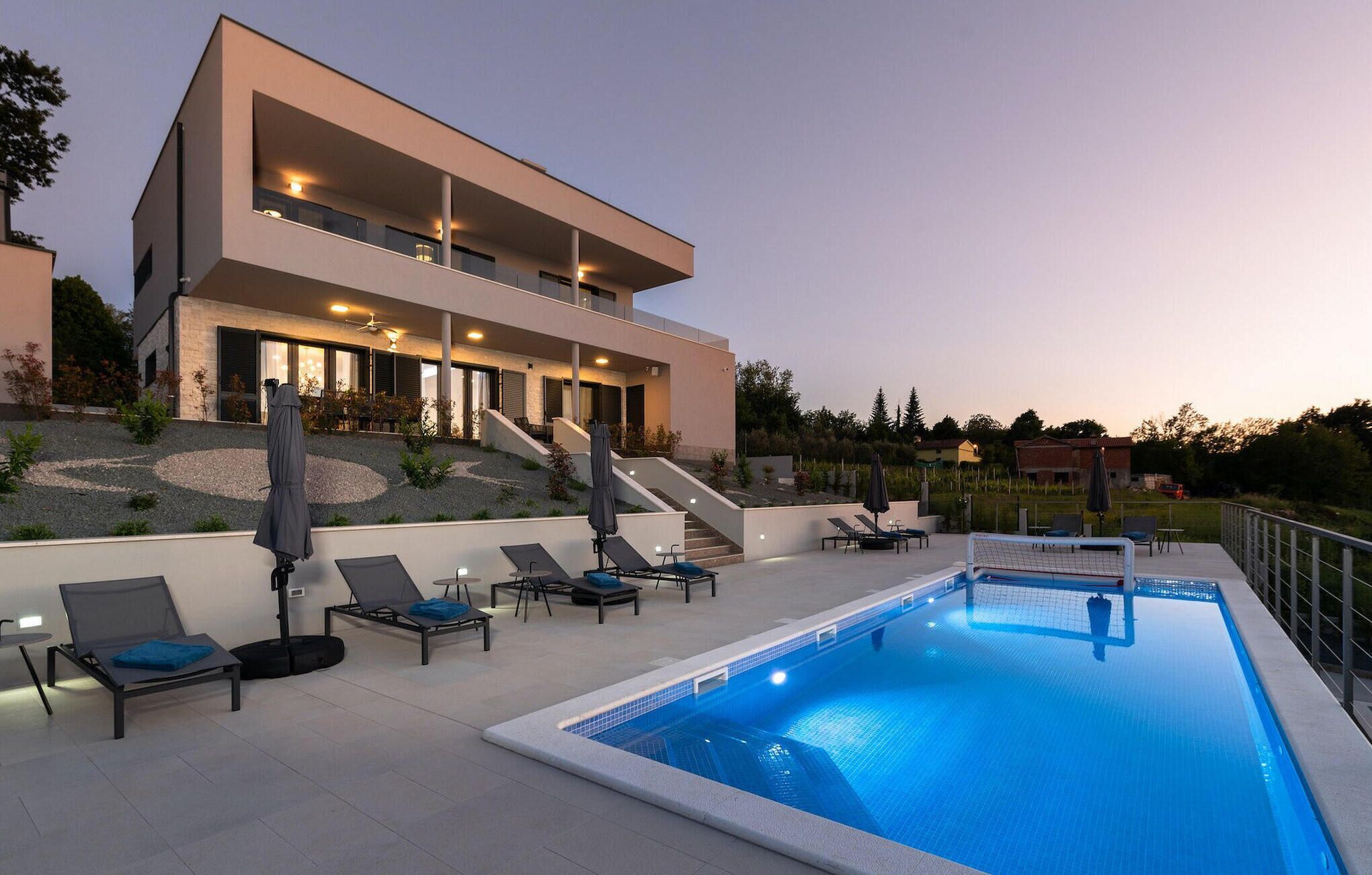 A modern two-story house with a swimming pool, outdoor seating, and a staircase leading to the upper floor.