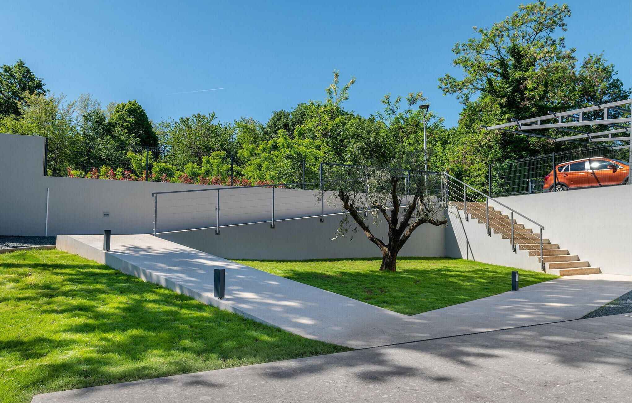 A modern outdoor area with a concrete pathway, a staircase, and a car parked nearby.