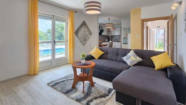 A modern living room with a grey sectional sofa, yellow cushions, a small wooden table with a plant, and a large window with yellow curtains. - Amazing home in Porec (Porec)