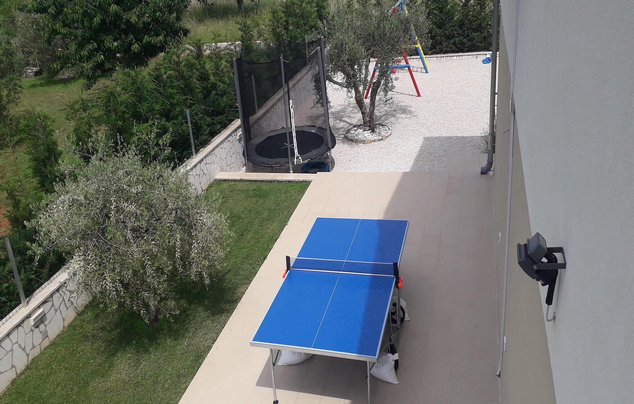 An outdoor ping pong table on a patio with a stone wall and greenery around.