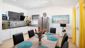 A modern kitchen with a dining area, featuring a large table with teal placemats, black chairs, and a decorative vase. - Amazing home in Porec (Porec)