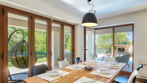 A dining area with a wooden table set for four, large windows, and a hanging chair. - Beautiful home in Umag (Umag)