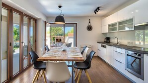 A modern kitchen with white cabinets, a built-in oven, and a dining area with a wooden table and chairs. - Beautiful home in Umag (Umag)