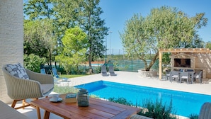 A poolside area with wicker furniture, a wooden table, and a barbecue setup. - Beautiful home in Umag (Umag)