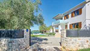 A modern two-story building with a stone wall entrance, a clear sky, and a view of a body of water. - Beautiful home in Umag (Umag)
