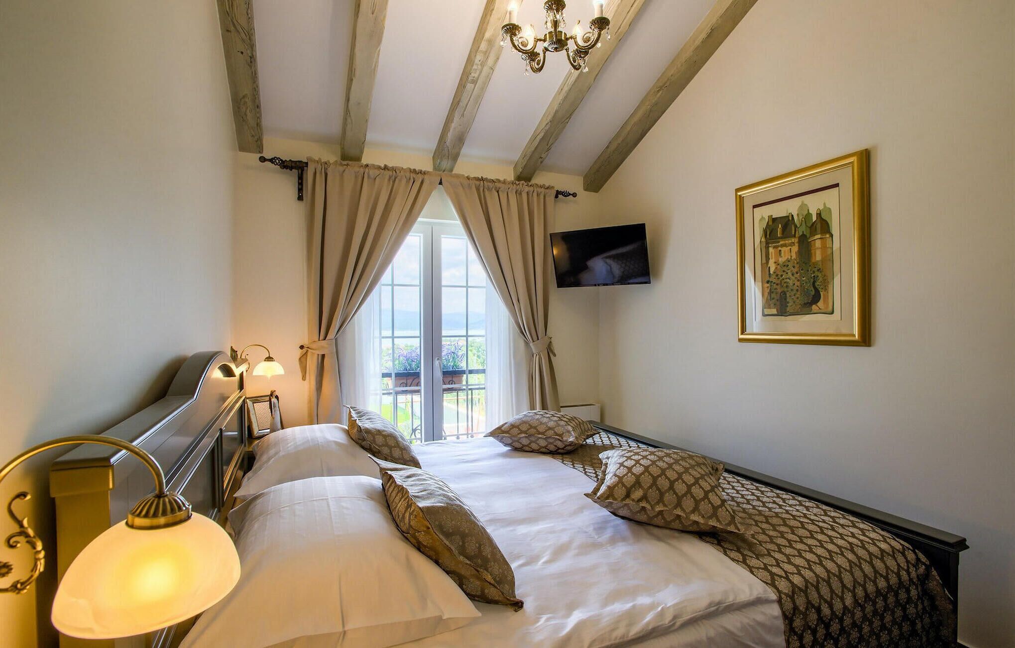 A bedroom with a bed, a TV mounted on the wall, and a window with curtains.
