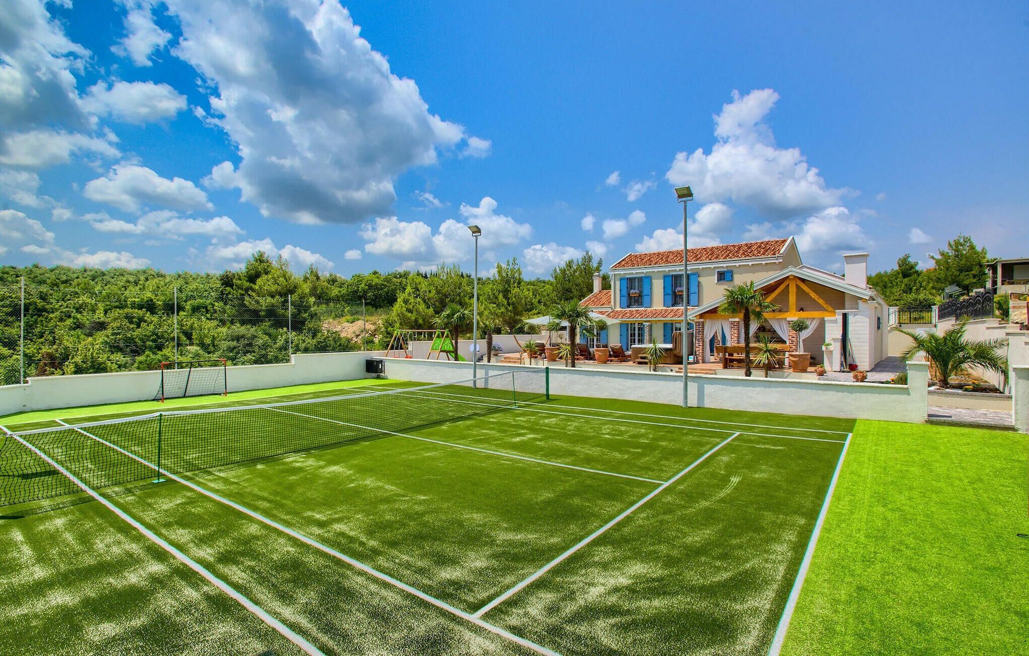 Un court de tennis avec un filet, entouré d’un mur blanc et d’une végétation luxuriante.