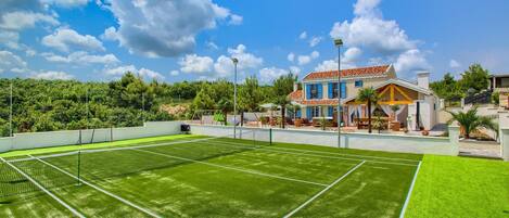Un court de tennis avec un filet, entouré d’un mur blanc et d’une végétation luxuriante.