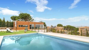 Une maison moderne dotée d’une piscine, d’un patio avec des chaises longues et offrant une vue sur le paysage environnant.