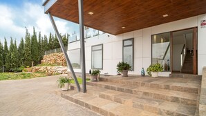 Un bâtiment moderne avec un escalier en pierre menant à une entrée constituée d’une porte en verre, le tout entouré de plantes en pot et d’un mur de pierre.