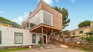 Une maison moderne dotée d’une structure en porte-à-faux originale, de grandes fenêtres et d’un mur de soutènement en pierre.