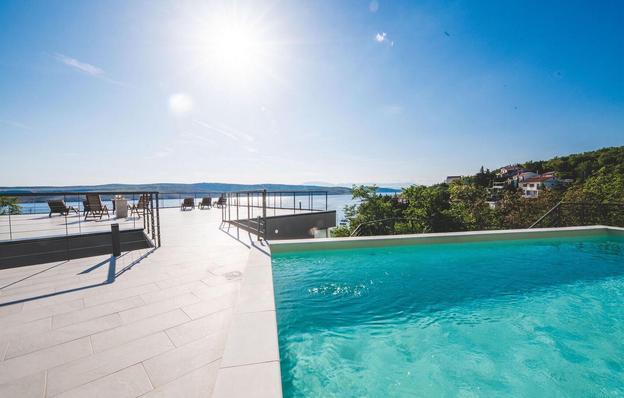 Ein Pool auf dem Dach mit klarem, blauem Wasser, umgeben von Liegestühlen und einem schönen Blick auf das Meer und die Hügel.