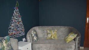 Un salon avec un canapé gris, deux coussins à motifs, une petite table d’appoint blanche et un sapin de Noël illuminé.