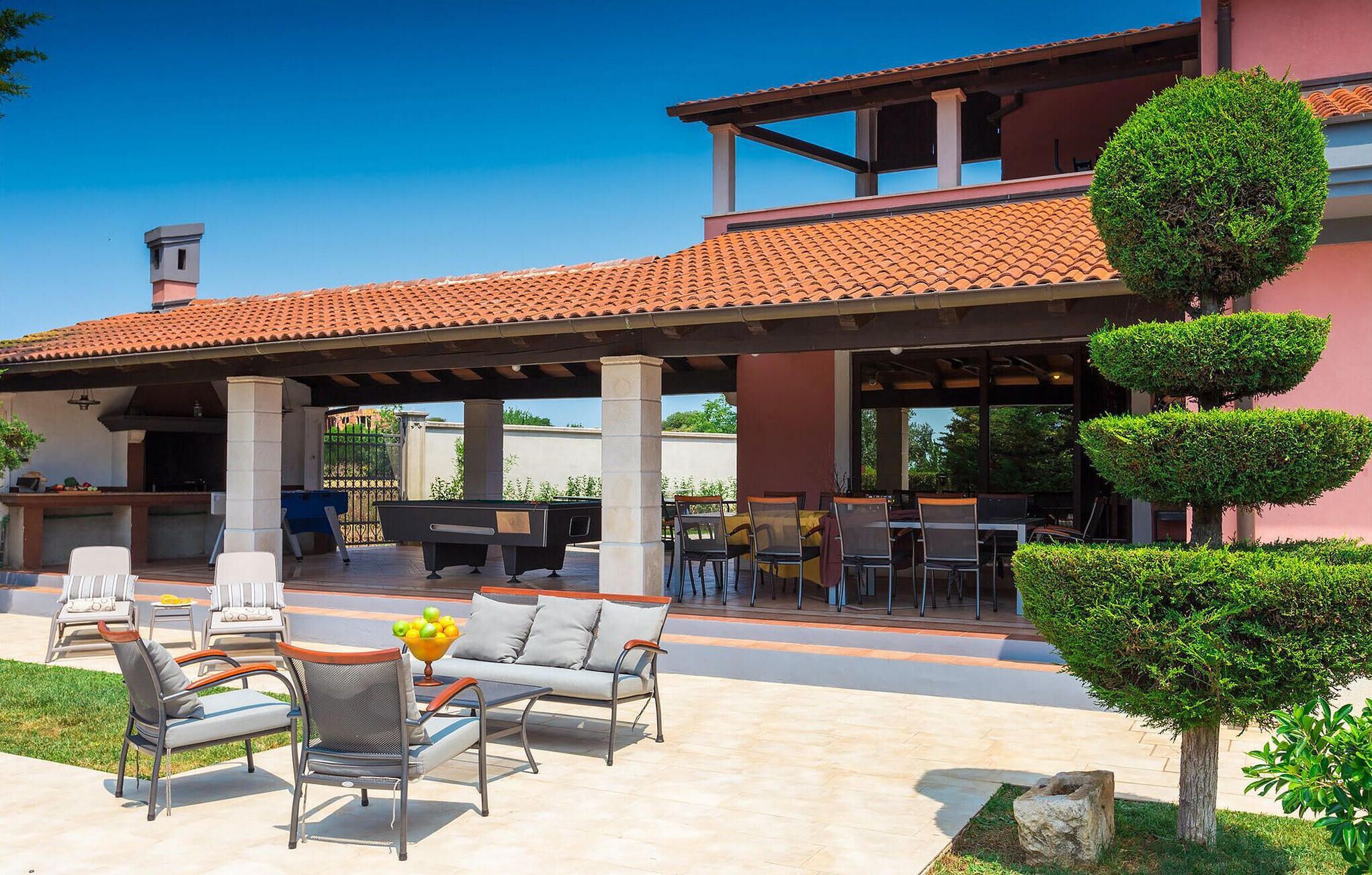 Un patio al aire libre con mesa de billar, sillas de descanso y zona de barbacoa.