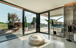 Un intérieur moderne avec de grandes portes-fenêtres coulissantes donnant sur une piscine, un pouf moelleux blanc et un style de décoration minimaliste.
