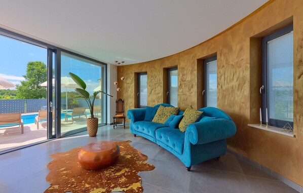 Un salon moderne avec un canapé bleu, une grande porte vitrée donnant sur une piscine et un tapis original en peau de vache.