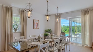 A dining area with a glass table, white chairs, and three hanging chandeliers. - Amazing home in Tinjan with sauna (Tinjan)