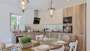 A modern kitchen with wooden cabinets, a built-in oven, and a dining area with a glass table set for four. - Amazing home in Tinjan with sauna (Tinjan)