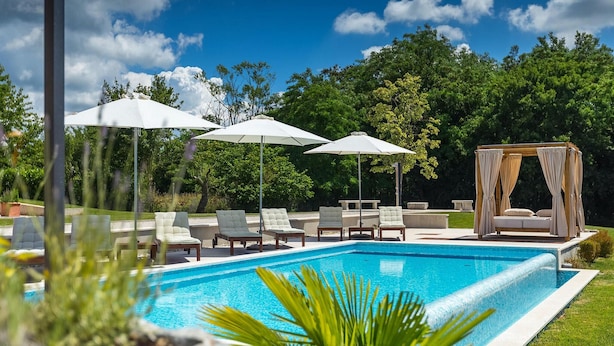 A swimming pool with lounge chairs and umbrellas, surrounded by greenery and a gazebo. - Amazing home in Tinjan with sauna (Tinjan)