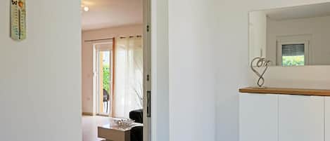 A hallway with a door leading to a room, a thermostat on the wall, and a decorative metal piece on a cabinet.