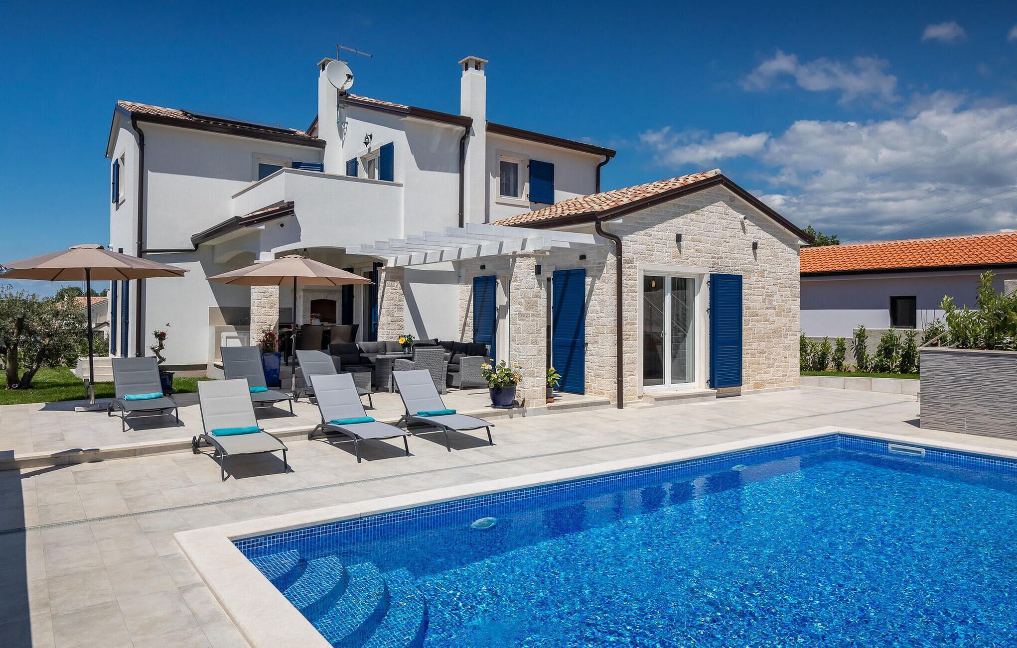 A modern two-story house with a swimming pool, outdoor seating, and a stone facade.