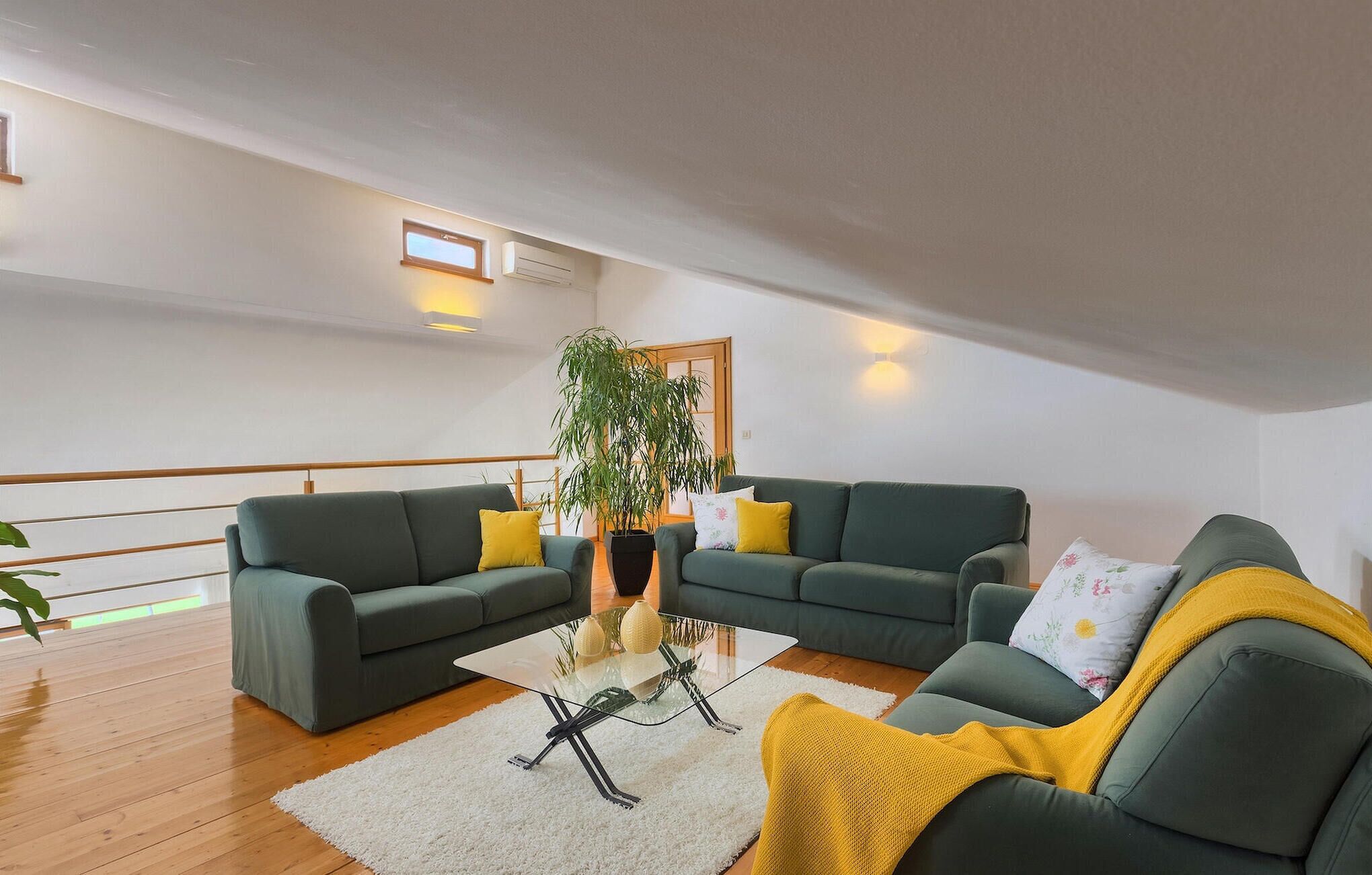 Uma sala de estar moderna com dois sofás verdes, uma mesa de centro de vidro e uma grande planta em vaso.