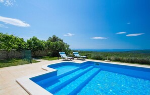 Relax by the serene pool with a clear view of the horizon, surrounded by lush greenery.