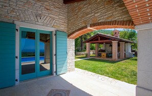 Relax in a serene outdoor space with a pergola, table, and chairs, surrounded by a lush lawn and a view of the pool.