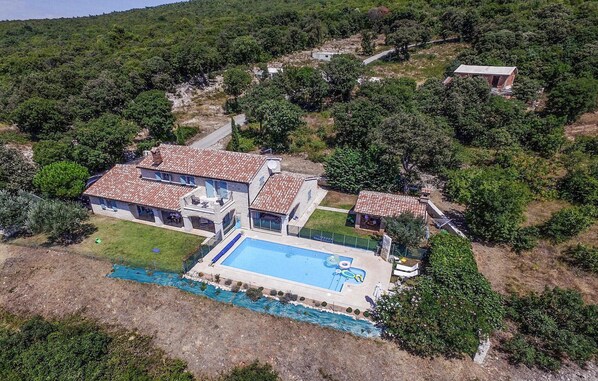 Enjoy a tranquil retreat in this villa surrounded by lush greenery and hills, featuring a spacious outdoor pool and multiple rooms.