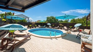 A swimming pool with lounge chairs and umbrellas, surrounded by a wooden deck and potted plants. - Beach front apartment in Peroj with WiFi (Peroj)