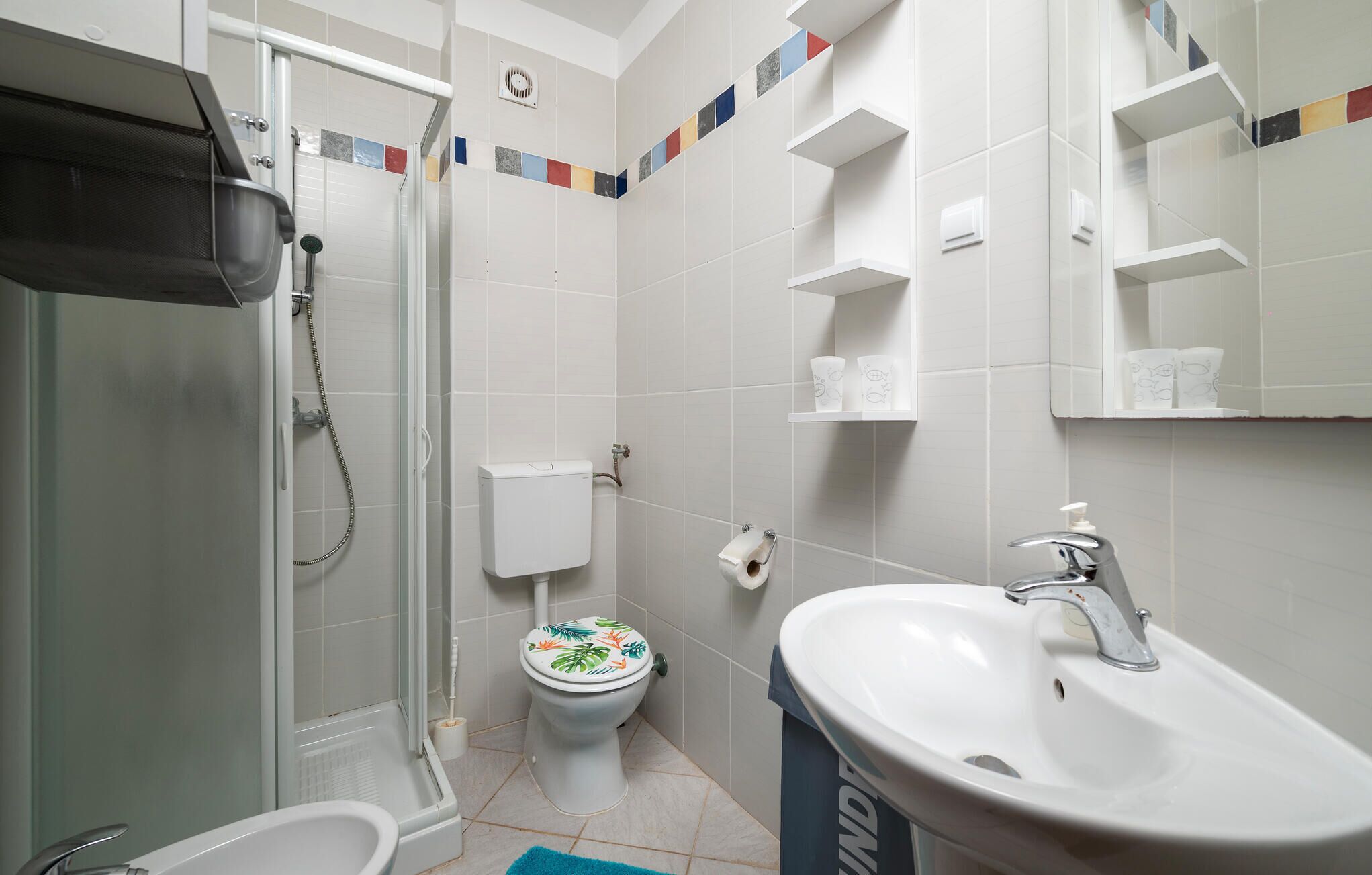 A bathroom with a shower, toilet, sink, and shelves.