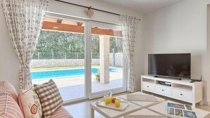 A living room with a TV, a sofa, a coffee table with drinks, and a view of a pool and garden. - Amazing home in Labin - Rabac (Labin - Rabac)